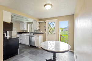 Kitchen with white cabinets, a textured ceiling, a sink, and dishwasher