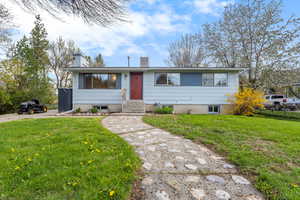 View of front of house featuring a front yard, fence, a chimney, and entry steps