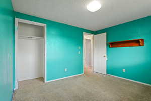 Unfurnished bedroom with a closet, baseboards, carpet flooring, and a textured ceiling