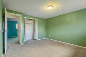 Unfurnished bedroom with carpet floors, a textured ceiling, baseboards, and a closet