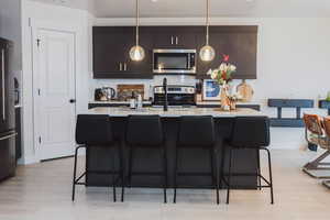 Kitchen with tasteful backsplash, decorative light fixtures, a breakfast bar, light countertops, and stainless steel appliances