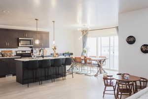 Kitchen with a kitchen bar, a notable chandelier, a center island with sink, stainless steel appliances, and light countertops