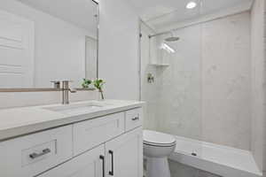 Bathroom with a marble finish shower, toilet, and vanity