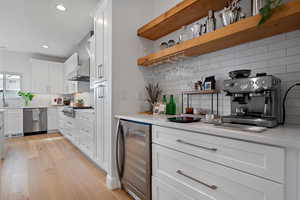 Kitchen with light wood-type flooring, beverage cooler, appliances with stainless steel finishes, white cabinets, and wall chimney range hood
