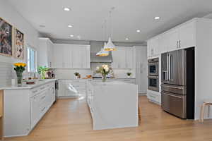 Kitchen featuring appliances with stainless steel finishes, a kitchen island, wall chimney exhaust hood, and light wood-style floors