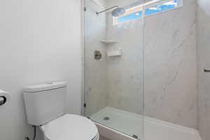 Full bathroom with a marble finish shower and toilet
