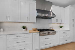 Kitchen featuring light wood-style floors, stainless steel gas stovetop, wall chimney exhaust hood, and light countertops
