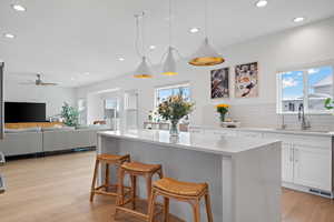 Kitchen with a wealth of natural light, light wood-style flooring, white cabinets, and a sink