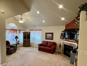Carpeted living area with lofted ceiling, a ceiling fan, and a tile fireplace