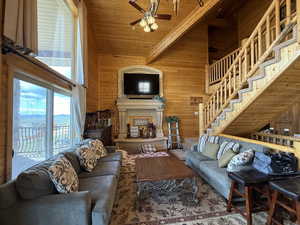 Living area with wooden walls, a ceiling fan, a fireplace with raised hearth, beamed ceiling, and a high ceiling