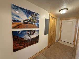 Corridor with electric panel, a textured ceiling, carpet flooring, and baseboards
