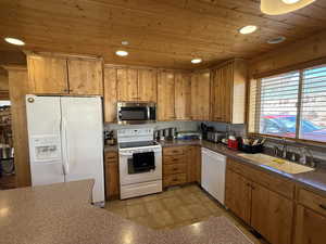 Kitchen featuring white appliances, a sink, wooden ceiling, dark countertops, and recessed lighting