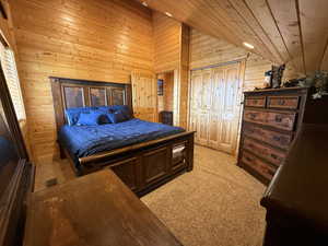 Bedroom with lofted ceiling, wood walls, light carpet, and wood ceiling