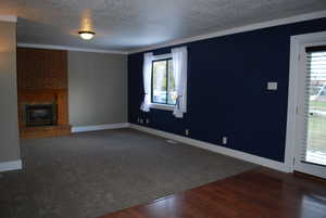 Unfurnished living room featuring a brick fireplace, carpet flooring, baseboards, and a textured ceiling