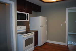 Kitchen with baseboards, white appliances, and dark wood-type flooring