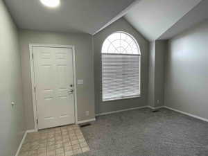 Foyer and living room with visible vents, new carpet, baseboards, and vaulted ceiling