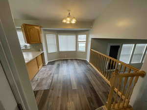 Unfurnished dining area featuring dark wood finished floors, stairway, a notable chandelier, and baseboards