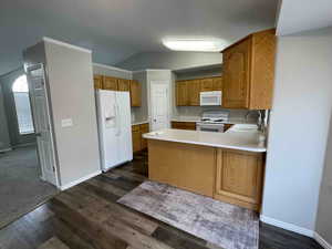 Kitchen featuring a sink, white appliances, a peninsula, light countertops, and vaulted ceiling