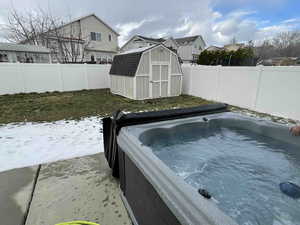 View of fenced backyard, a hot tub, a storage shed, and a residential view