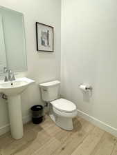 Half bathroom with toilet, baseboards, and wood finished floors