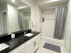 Basement full bathroom with tile patterned flooring, visible vents, shower / tub combo with curtain, double vanity, and a sink