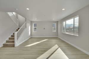 Unfurnished living room with recessed lighting, baseboards, stairs, and light wood-style floors
