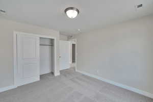 Unfurnished bedroom featuring a closet, visible vents, light colored carpet, and baseboards