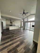 Kitchen open to  family  room with a ceiling fan, dark wood-style floors, baseboards, lofted ceiling and gas fireplace.