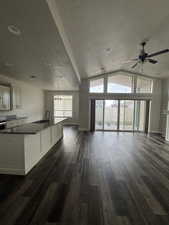 Kitchen open to  family  room with a ceiling fan, dark wood-style floors, baseboards, lofted ceiling and gas fireplace.