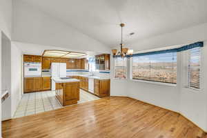 Kitchen with white appliances, brown cabinetry, visible vents, and a chandelier