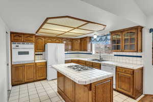 Kitchen with a sink, white appliances, tasteful backsplash, and brown cabinets