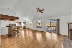 Living room with light wood finished floors, visible vents, vaulted ceiling, a fireplace, and a ceiling fan