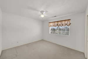 Carpeted empty room with visible vents, baseboards, a textured ceiling, and a ceiling fan