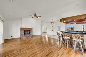 Interior space with lofted ceiling, light wood-style floors, a brick fireplace, and a ceiling fan