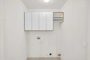 Clothes washing area featuring a textured ceiling, hookup for a gas dryer, cabinet space, baseboards, and hookup for a washing machine