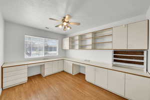 Unfurnished office with a ceiling fan, visible vents, built in desk, and light wood finished floors