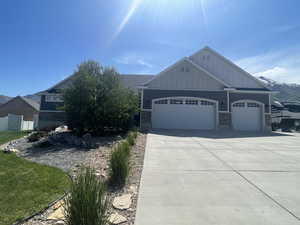 View of front of house featuring board and batten siding, a garage, driveway, and stone siding