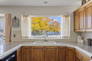 Kitchen featuring brown cabinets, backsplash, dishwashing machine, and tile counters