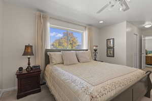 Bedroom with light colored carpet, ensuite bathroom, ceiling fan, and a textured ceiling