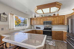 Kitchen featuring a peninsula, brown cabinetry, stainless steel appliances, decorative backsplash, and a textured ceiling