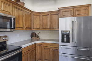 Kitchen featuring stainless steel appliances, brown cabinets, backsplash, and tile counters