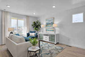 Living room with visible vents, baseboards, recessed lighting, light wood-style flooring, and a textured ceiling