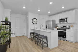 Kitchen with light wood-type flooring, appliances with stainless steel finishes, a kitchen breakfast bar, white cabinetry, and a sink