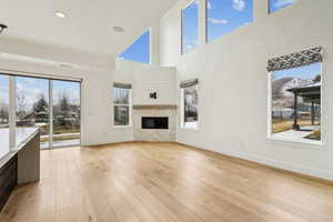 Living room featuring a glass covered fireplace, light wood-type flooring, baseboards, and a towering ceiling