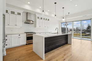 Kitchen with a sink, wall chimney range hood, light wood-type flooring, and stainless steel appliances