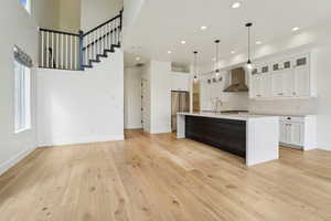 Kitchen with light wood-type flooring, a sink, wall chimney range hood, light countertops, and high end refrigerator