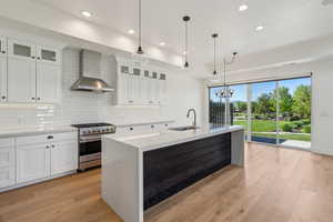Kitchen featuring high end stainless steel range, wall chimney exhaust hood, a sink, tasteful backsplash, and light wood-style floors