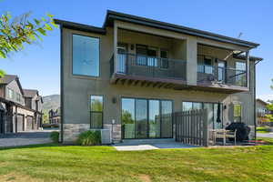 Rear view of property with a balcony, stone siding, stucco siding, central AC, and a patio area
