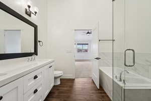 Bathroom featuring wood tiled floor, toilet, a tub to relax in, double vanity, and a sink