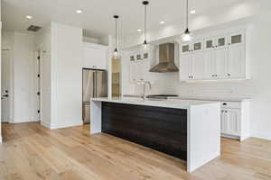 Kitchen with visible vents, light wood-style flooring, a sink, high end refrigerator, and wall chimney range hood